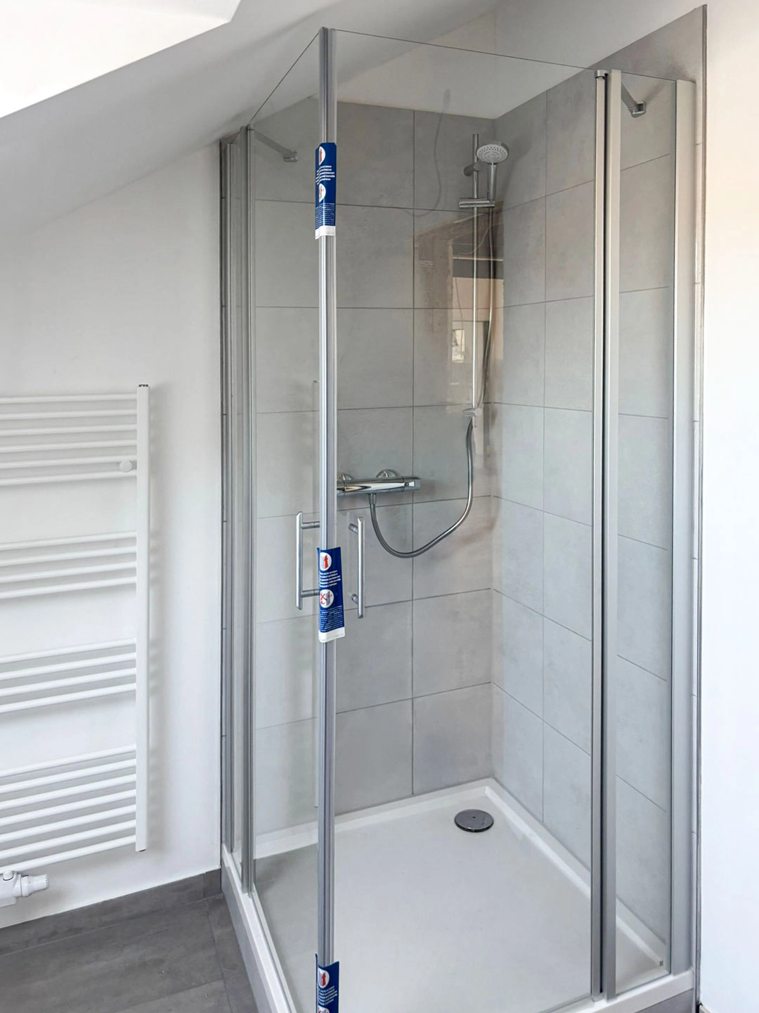 Neues Bad im Dachgeschoss Loft mit moderner Dusche, Glasabtrennung und hellen Fliesen nach Sanierung.