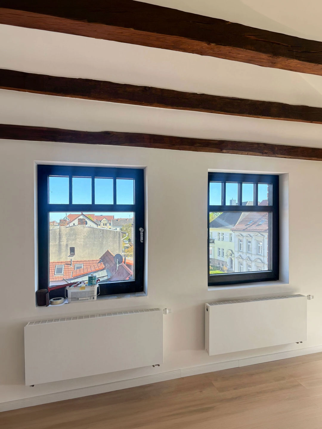 Neue Fenster im sanierten Dachgeschoss Loft mit sichtbaren Holzbalken und Blick über die Altstadt.
