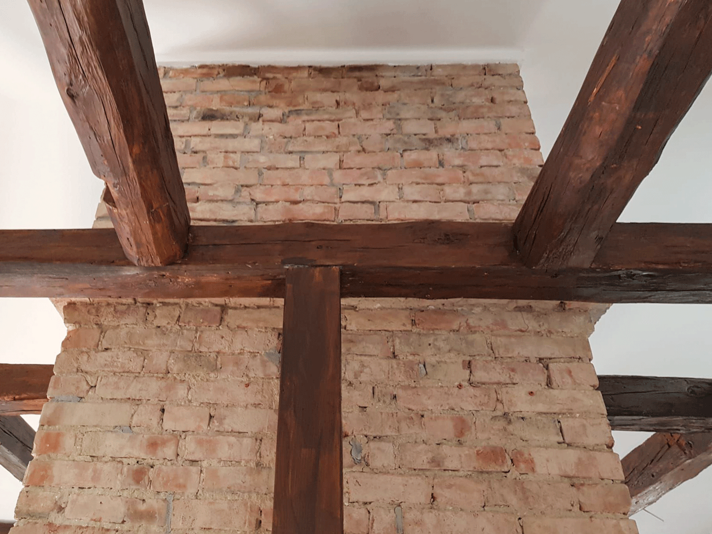 Freigelegte Steinmauer im Loftdachgeschoss mit sanierten Holzbalken und sichtbarem Dachstuhl.