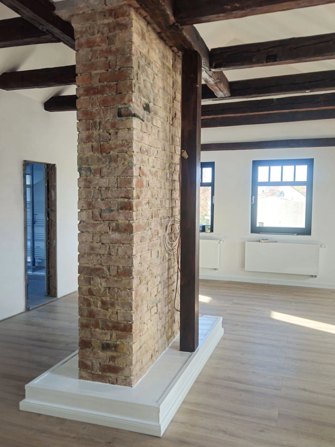 Freigelegte Ziegelstützwand im Dachgeschoss Loft mit sanierten Holzbalken, neuen Fenstern und hellem Ausbau.